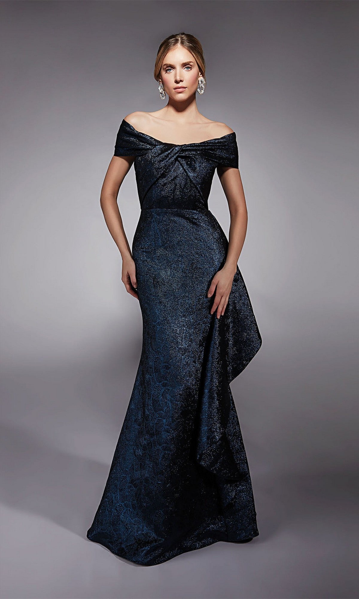 A woman poses against a plain gray background wearing the Alyce 27774 long formal dress in navy, featuring an off-the-shoulder neckline, fitted bodice, side draping, and a flared mermaid skirt.